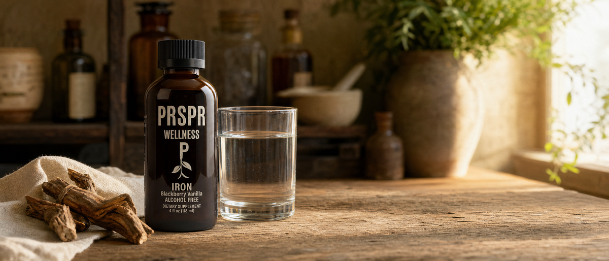 PRSPR Wellness Liquid Iron bottle on a wooden table beside a glass of water and dried root pieces