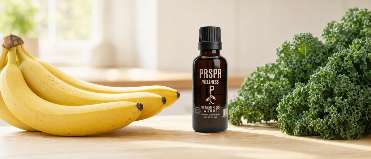 PRSPR Vitamin D3 with K2 dropper bottle on a kitchen table between a bunch of bananas and a bunch of curly kale