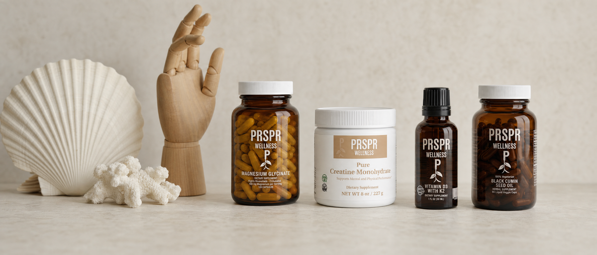 Four PRSPR Wellness supplements from the Essentials Bundle on a limestone table beside a white scallop shell, white coral and a wooden jointed hand model