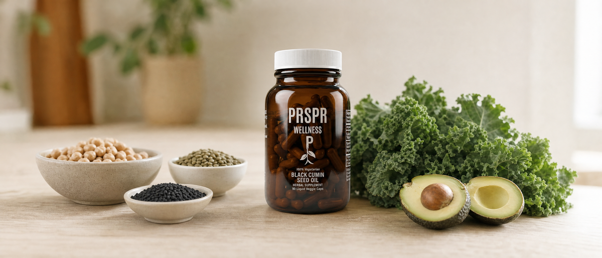 PRSPR Wellness Black Cumin Seed Oil veggie caps on a kitchen table beside bowls of chickpeas, lentils and nigella seeds, kale and avocado