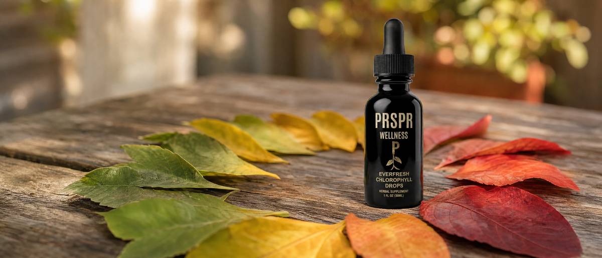 A PRSPR Wellness Everfresh Chlorophyll Drops bottle on a weathered wooden table surrounded by autumn leaves that change color from green to yellow, orange and red