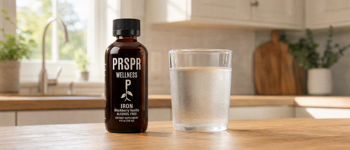 PRSPR Wellness Liquid Iron blackberry vanilla dropper bottle on a kitchen counter next to a glass of water