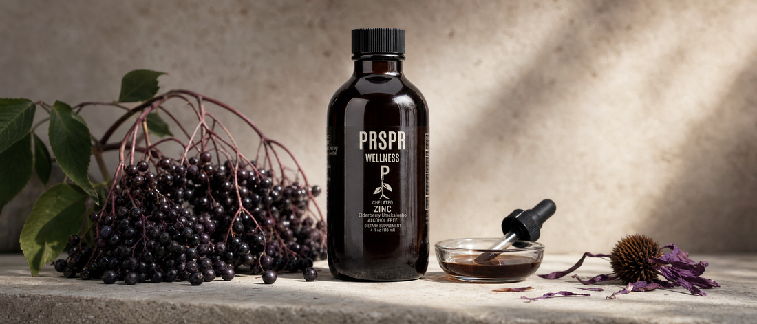 PRSPR Chelated Zinc with Elderberry bottle on stone beside a cluster of dark elderberries and dried purple coneflower petals