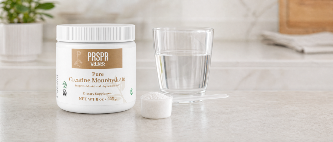 PRSPR Wellness Pure Creatine Monohydrate tub on a stone kitchen counter beside a scoop and a glass of water