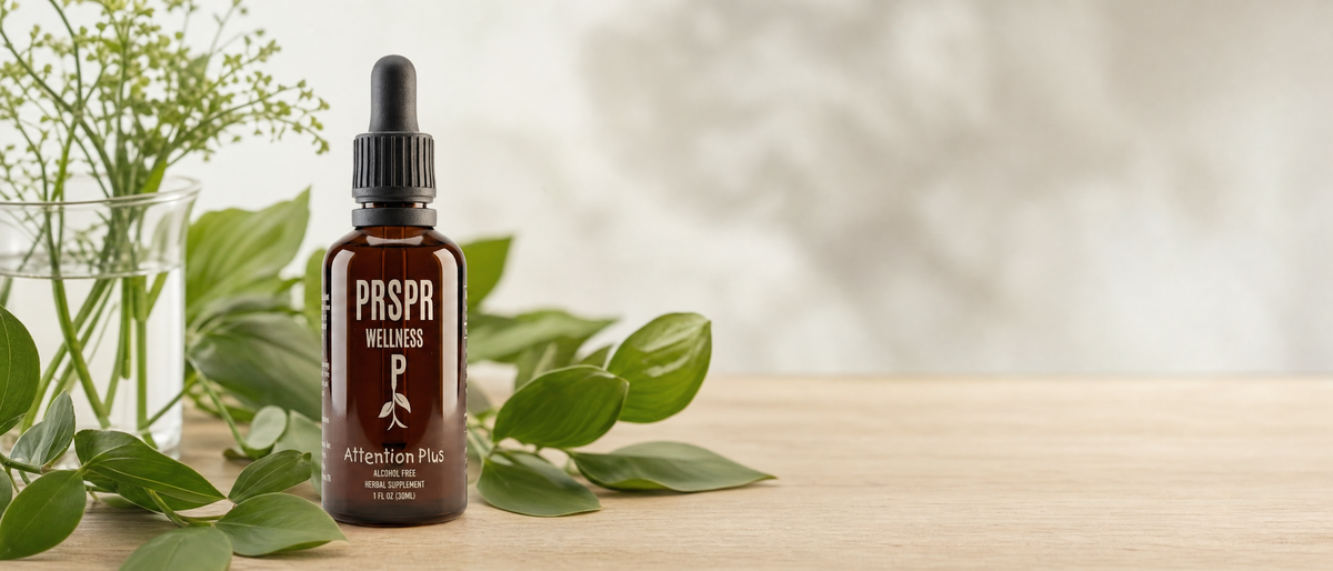 PRSPR Wellness Attention Plus botanical liquid dropper bottle on a light wooden table surrounded by green leaves