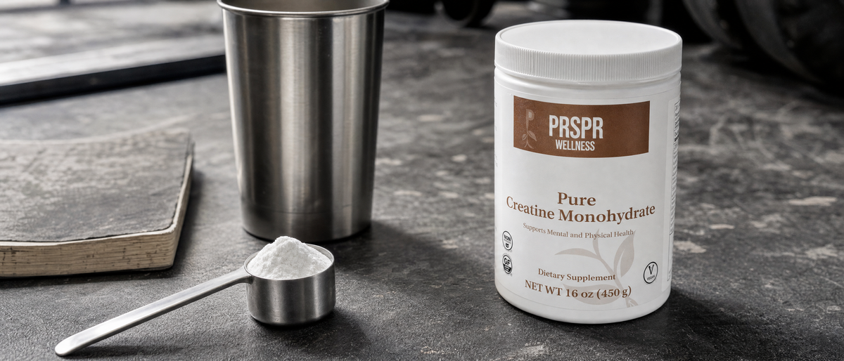 PRSPR Wellness Pure Creatine Monohydrate tub on grey gym flooring beside a steel scoop, shaker cup and closed notebook