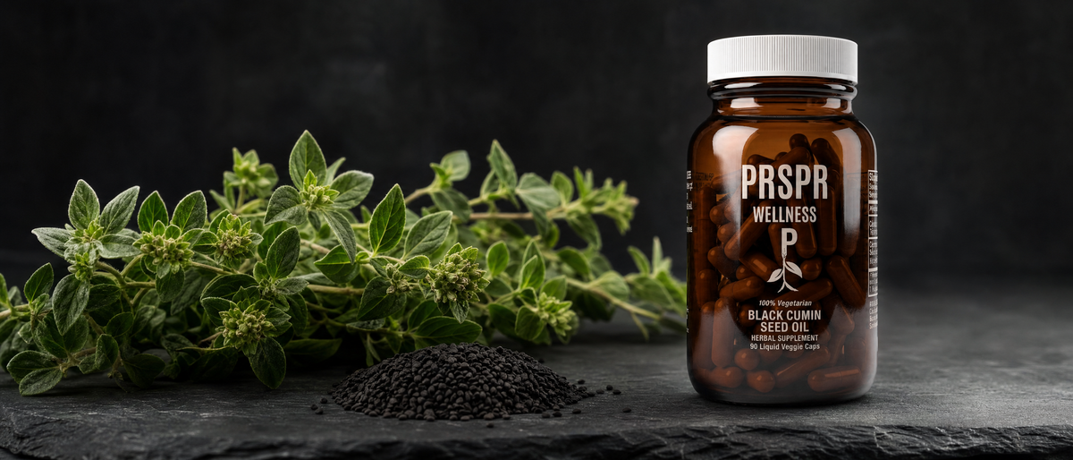 PRSPR Wellness Black Seed Oil bottle on dark slate beside a separate bundle of fresh oregano sprigs and a heap of black seeds