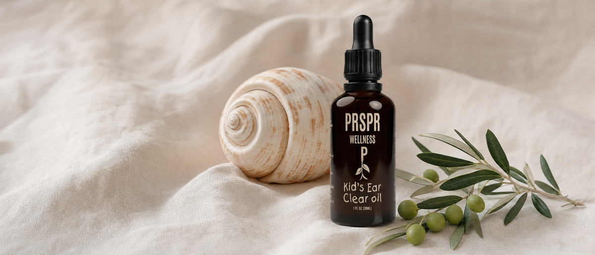 Kid's Ear Clear Oil dropper bottle on natural linen beside a spiral seashell and an olive branch with green olives