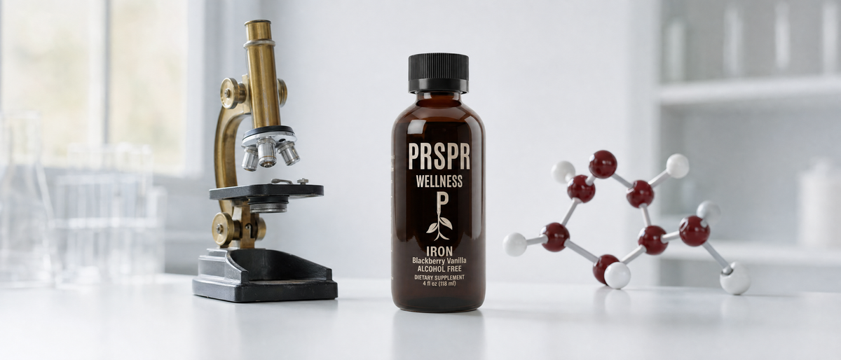 PRSPR Wellness Liquid Iron bottle on a white lab bench between a brass microscope and a red and white molecular model