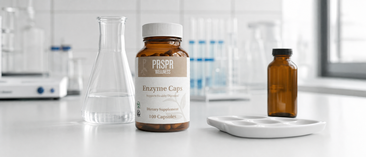 PRSPR Enzyme Caps bottle on a chemistry lab bench beside a glass flask of clear liquid, a porcelain spot plate and an amber reagent bottle
