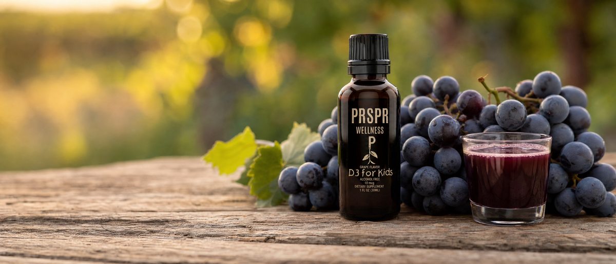 PRSPR D3 for Kids grape flavor dropper bottle on a rustic table beside a bunch of dark Concord grapes and a glass of grape juice