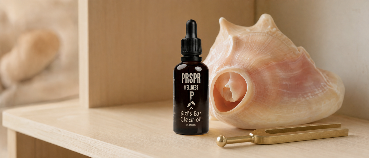 PRSPR Kid's Ear Clear Oil dropper bottle on a wooden shelf beside a conch shell and a brass tuning fork