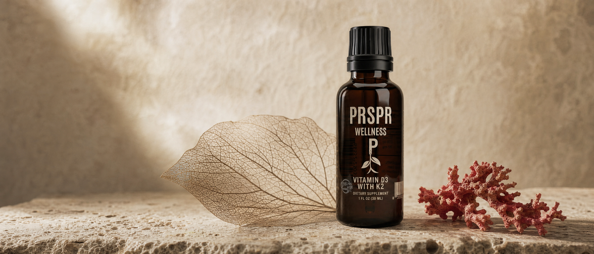 PRSPR Wellness Vitamin D3 with K2 dropper bottle on stone beside a skeleton leaf with branching veins and a piece of red coral
