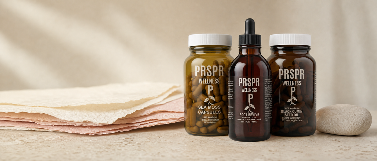 The PRSPR Wellness Hair & Skin Stack, Sea Moss Capsules, Root Revive and Black Cumin Seed Oil, on pale stone beside layered sheets of cream and pink handmade paper