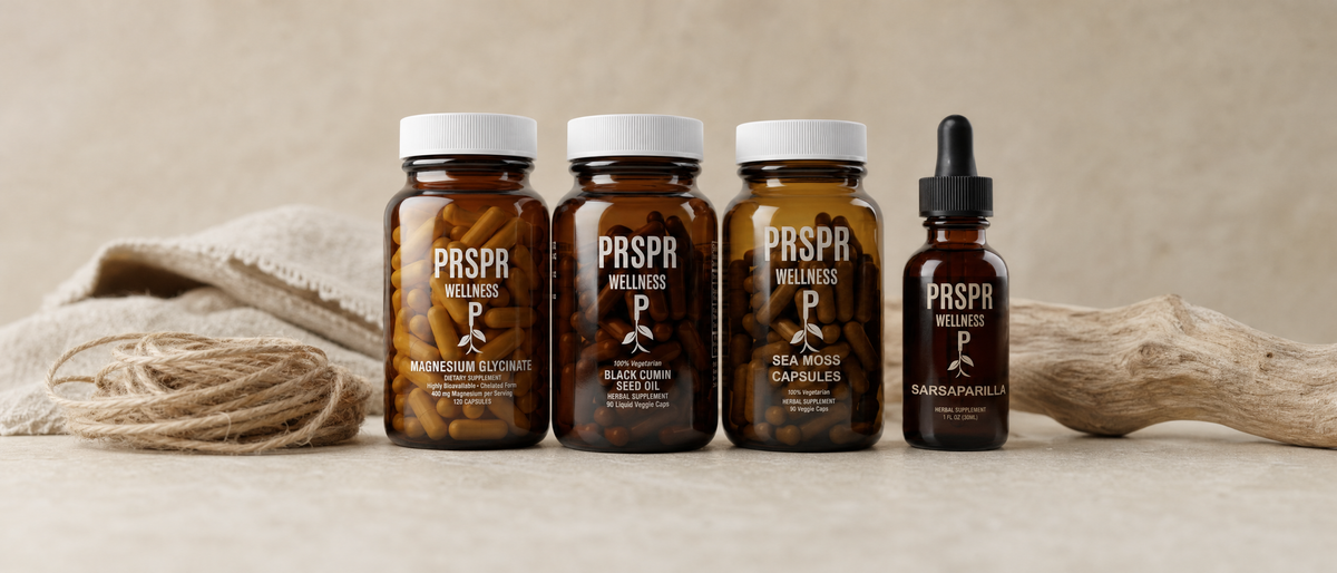 Amber jars of Magnesium Glycinate, Black Cumin Seed Oil and Sea Moss Capsules and a Sarsaparilla dropper bottle on pale limestone beside jute twine, frayed woven linen and driftwood