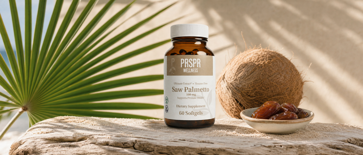 A PRSPR Wellness Saw Palmetto softgel jar on sandy driftwood beside a green fan-shaped palm frond, a whole husked coconut and a small dish of dates.