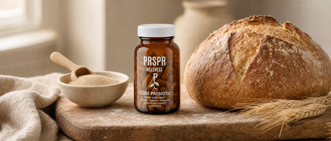 PRSPR Wellness FLORÉ Probiotic amber capsule jar on a floured oak bread board beside a crusty loaf, a bowl of dry yeast granules with a wooden scoop and wheat ears.